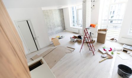 Grand salon lumineux et vide en phase de finition pour rénover un appartement avec un sol clair et un pilier en briques blanches